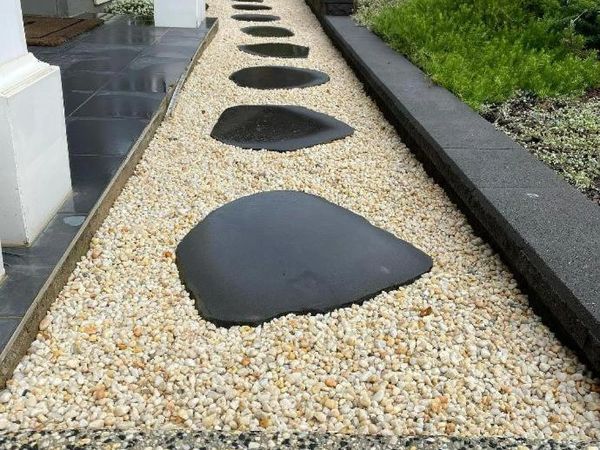 Pathway with large black stones on white gravel between garden and tiled floor.