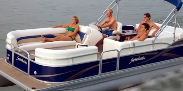 Four people relaxing on a blue and white pontoon boat on calm water.