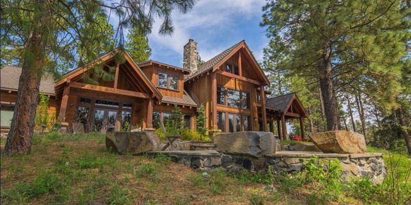 Rustic wooden cabin surrounded by pine trees under a blue sky.