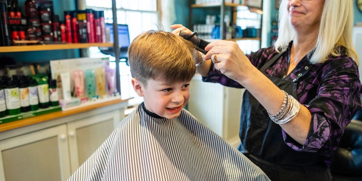 Woman cutting hair of the toddler on the salon