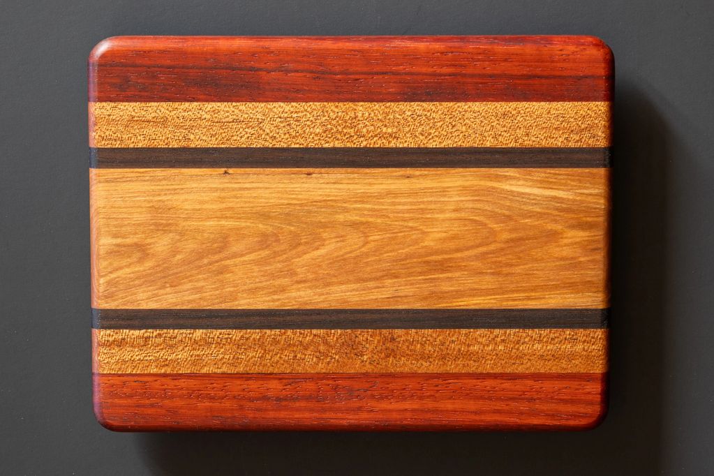 Rectangular wooden cutting board with multiple wood tones and smooth edges.