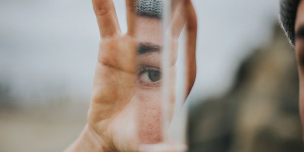 a hand holding a mirror reflecting on a person who is not seen except for their eye in the reflectio