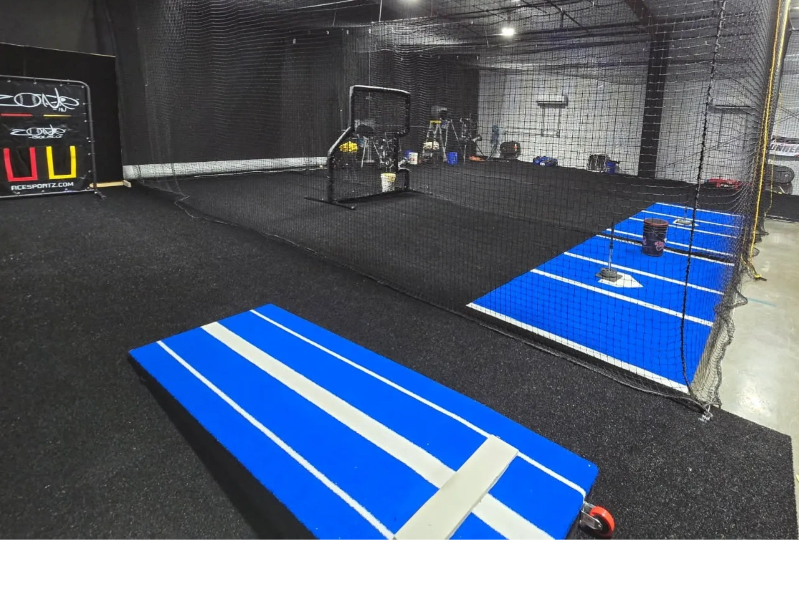 Indoor baseball training facility with pitching mounds and nets.