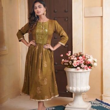 Woman in a golden-brown dress posing indoors near flowers.