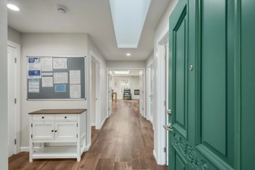 View from an open green door into a bright hallway with wooden floors and white walls.