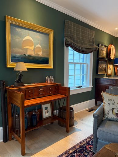 Room with green walls and antique desk with roman shades 