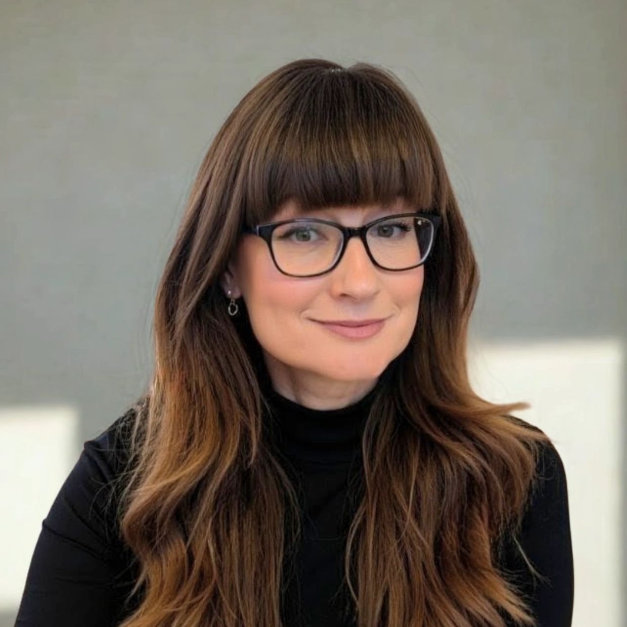 A woman with long brown hair and glasses smiling softly.