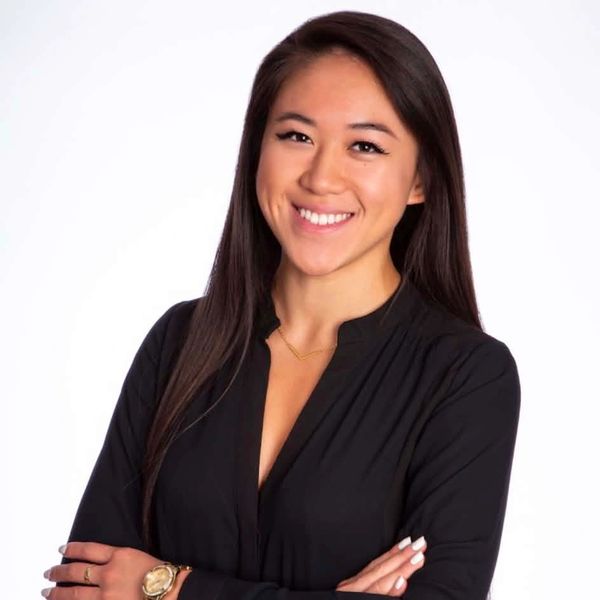 Confident woman in black blouse smiling with arms crossed against white background.