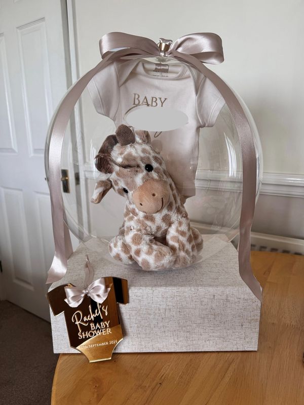 Baby shower gift with plush giraffe and onesie in clear balloon.