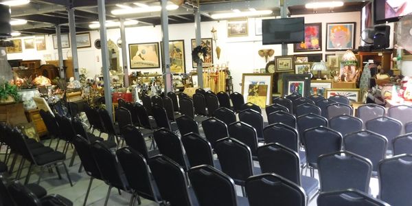 Rows of empty chairs set up in front of various paintings and antiques.