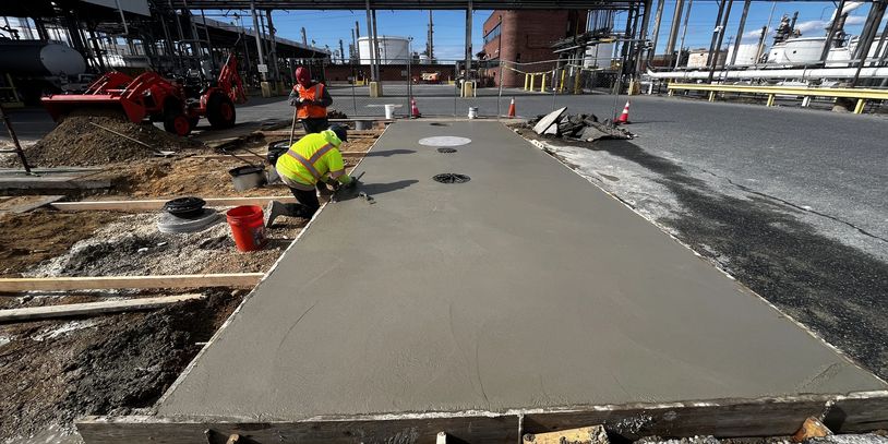 Workers smoothing wet concrete outdoors at a construction site.