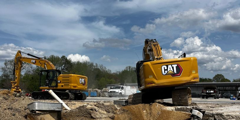 Two CAT excavators at a construction site under partly cloudy sky.