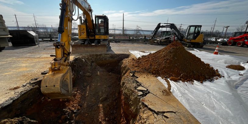 Excavator digging at a construction site with dirt pile.