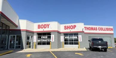Exterior view of Thomas Collision Body Shop with clear signage and a parked black truck.