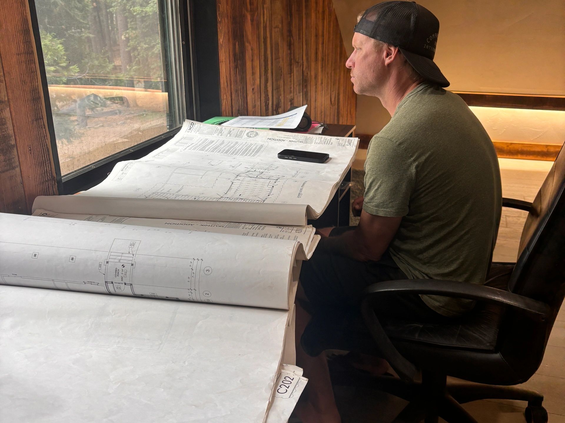 A man studies blueprints by a window.