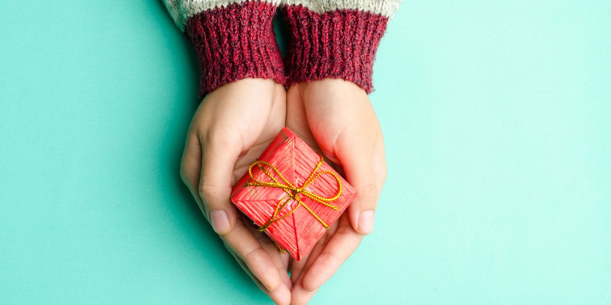 Small red gift box held in hands put together on Givelist wish lists about page.