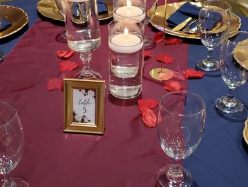 Elegant table setting with candles, rose petals, and a table number card.