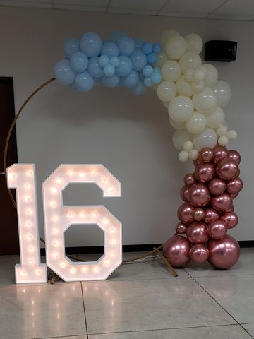 Illuminated number 16 with a balloon arch in blue, white, and rose gold colors.