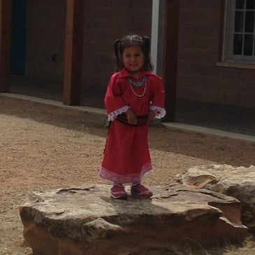 A young girl in a red dress stands on a large rock outdoors.