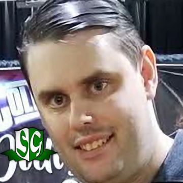 Close-up of a man smiling with slicked-back hair.