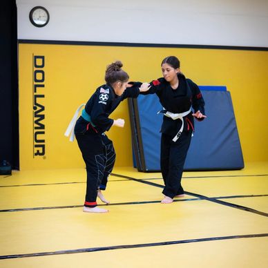 Two young martial artists practicing sparring in a dojo with yellow mats.