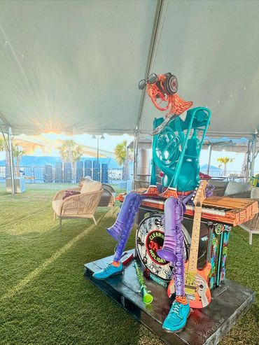 Colorful metal sculpture of a person with headphones sitting on a drum under a tent.