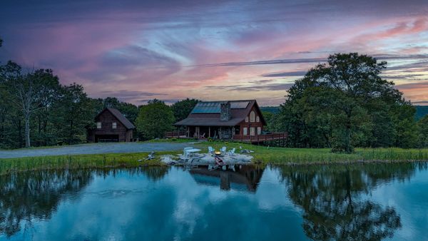 Lakeside cabin at sunset with colorful sky reflection.