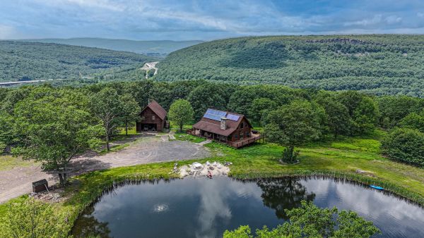 Rustic cabins near a tranquil pond surrounded by lush green hills and forests.