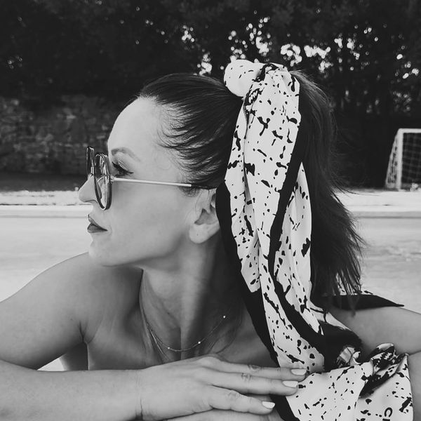 Frau mit Sonnenbrille und Schal im Haar schaut seitlich.