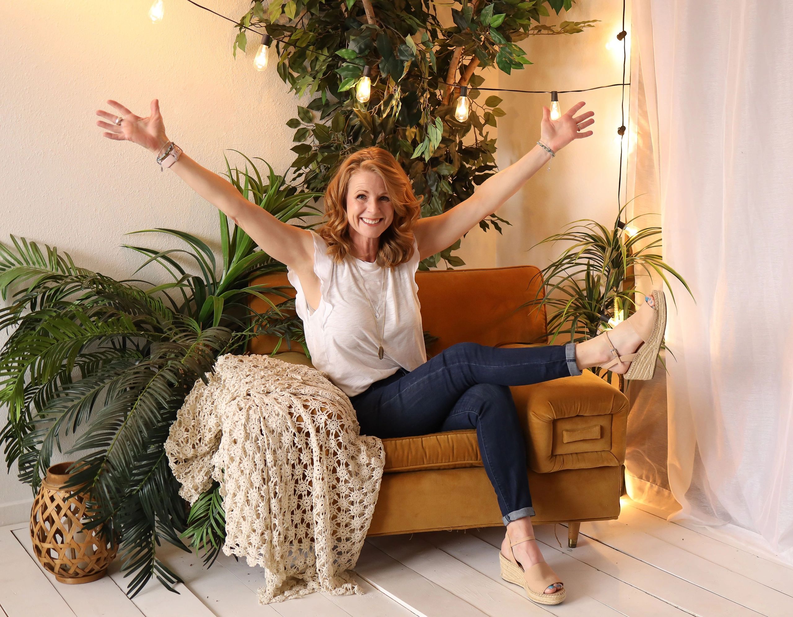 Siouxsie Przytulski the holistic health & life coach sitting on a couch with plants, lights and a bl