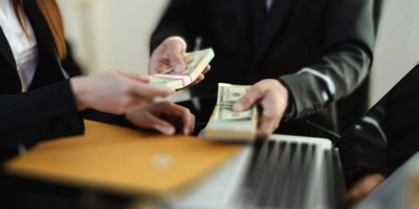 Businesspeople exchanging large stacks of cash during a meeting.