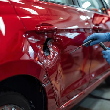 A damaged red car door being repaired by a technician.