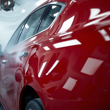 Close-up of a glossy red car door reflecting lights.