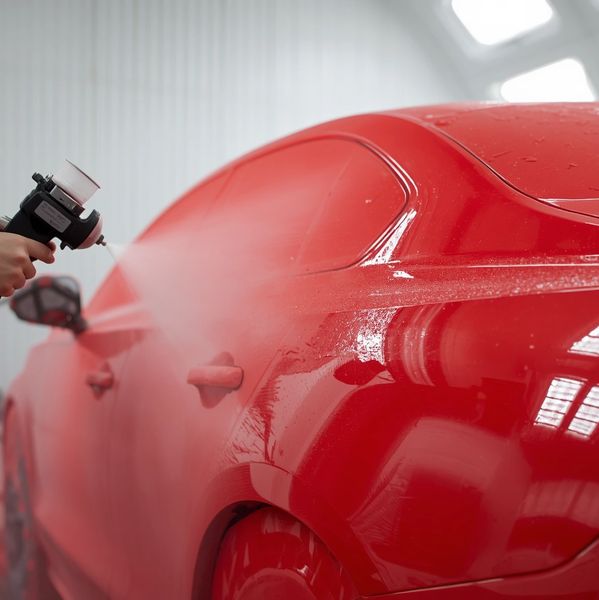 A red car being spray painted in a workshop.