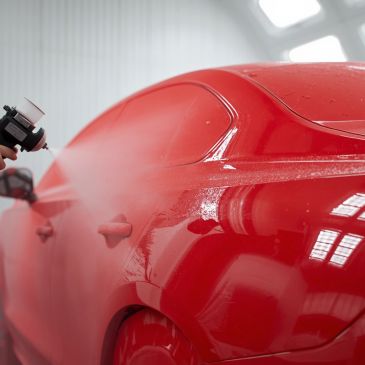 A red car being spray painted in a workshop.