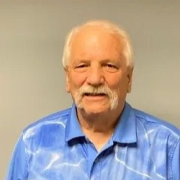 Smiling elderly man with white hair and mustache wearing a blue shirt.