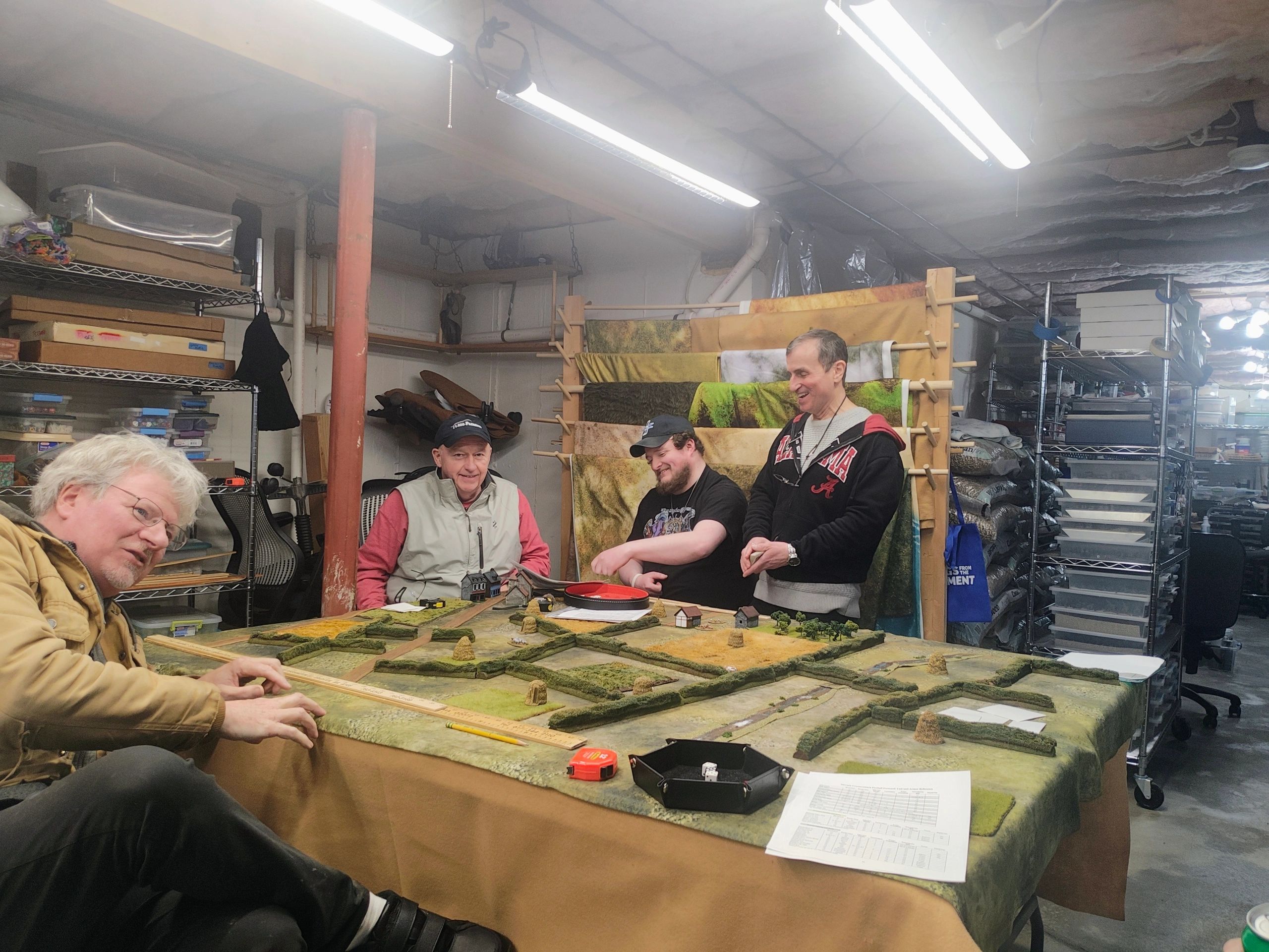 Four men playing tabletop war game in a basement room.