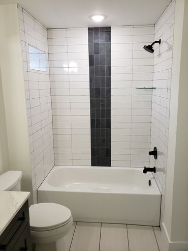 Modern bathroom with white tiles and black vertical accent in shower area.