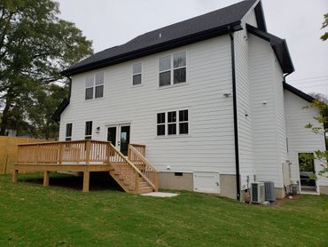 A modern two-story white house with a wooden deck and green lawn.