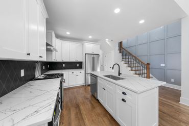 Modern white kitchen with marble countertops and wooden floors.