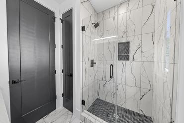 Modern bathroom shower with glass door and marble tiles.