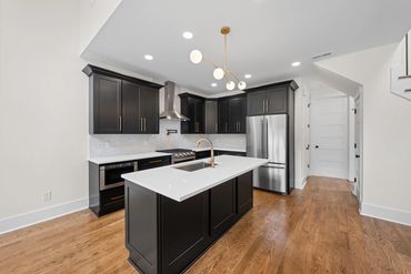 Modern kitchen with black cabinets, white countertops, and wooden floors.