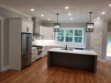 Modern kitchen with white cabinets, dark island, and hardwood floors.