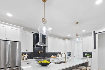 Modern kitchen with white cabinets, black backsplash, and marble island.