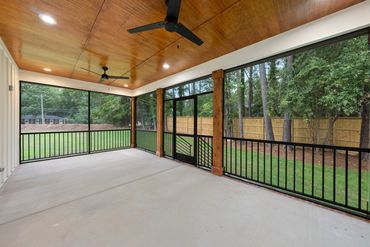 Spacious screened porch with wooden ceiling and ceiling fans overlooking a green backyard.
