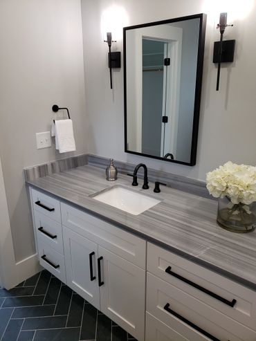 Modern bathroom vanity with gray countertop, black fixtures, and white cabinetry.