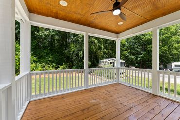 Cozy wooden porch with white railings overlooking a green backyard.