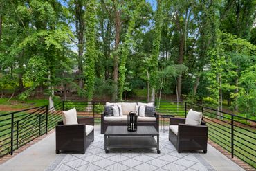 Cozy outdoor patio set with sofa and chairs surrounded by lush green trees.