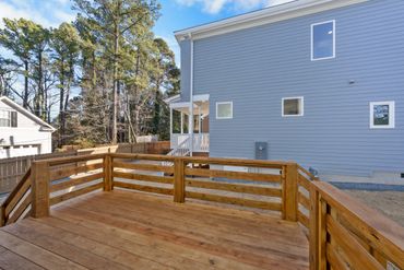 Spacious wooden deck attached to a modern blue house with surrounding trees.