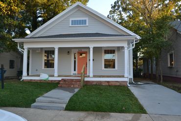A cozy gray house with a red door and front porch.